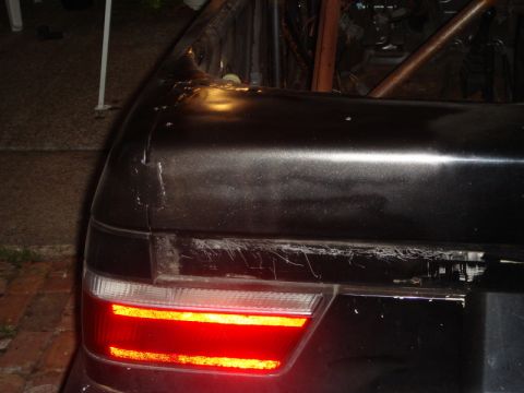 1989 Ford Escort - Rear view of a dark vehicle showing damage to the trunk lid and a red taillight.