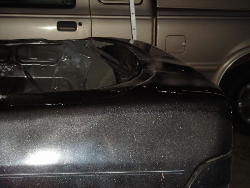 Close-up of a dark metallic car fender with a silver truck visible behind it