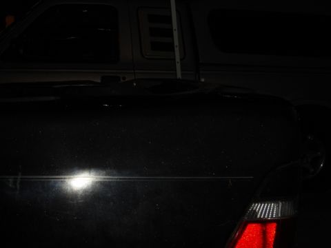 1989 Ford Escort - A dark-colored truck is partially visible from the side, with another vehicle behind it in the background.