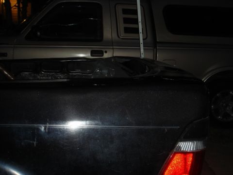 1989 Ford Escort - The rear of a dark-colored car is visible, with a silver pickup truck parked behind it.