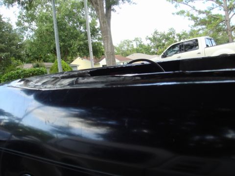 1989 Ford Escort - The foreground shows the damaged edge of a black car's roof, with a white pickup truck visible in the background.
