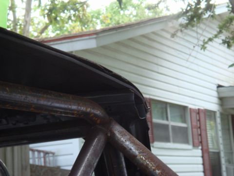 1989 Ford Escort - Close-up view of a rusty roll cage and the edge of a car's roof against a house.