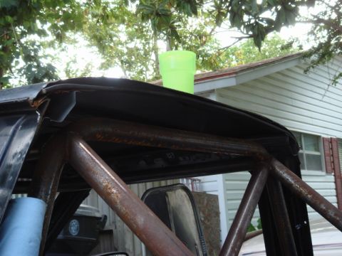 1989 Ford Escort - A rusty roll cage is visible inside a vehicle, with a green cup perched on the roofline.