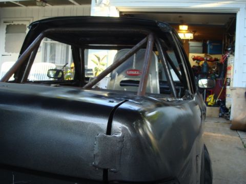 1989 Ford Escort - The interior of a car shows a roll cage and a racing seat, with a garage visible in the background.