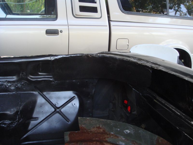 Underside of a car with black undercoating and a silver pickup truck in the background