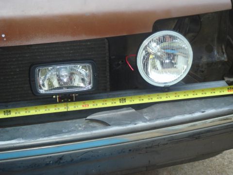 1989 Ford Escort - A tape measure is used to show the dimensions of auxiliary lights mounted on the front of a vehicle.