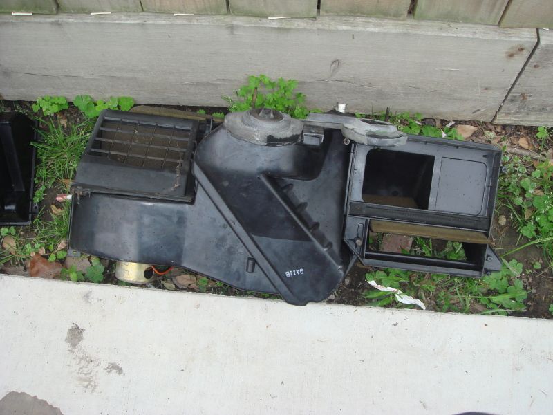 Black plastic HVAC blower motor housing with vents and a metal fan shroud, lying on the ground