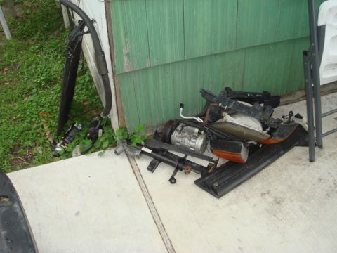 1989 Ford Escort - Assorted car parts are piled up outdoors next to a building.
