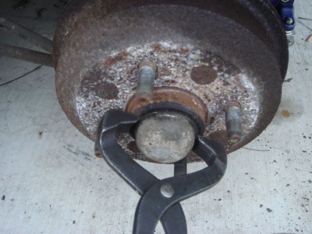 pliers gripping a ball joint on a rusty brake drum