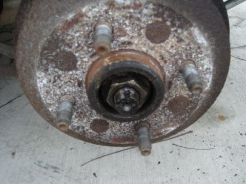 1989 Ford Escort - Close-up view of a rusted wheel hub assembly, showing the lug bolts and central nut.