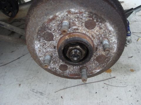 1989 Ford Escort - Close-up of a rusty wheel hub and brake drum assembly, showing lug studs and a central nut.