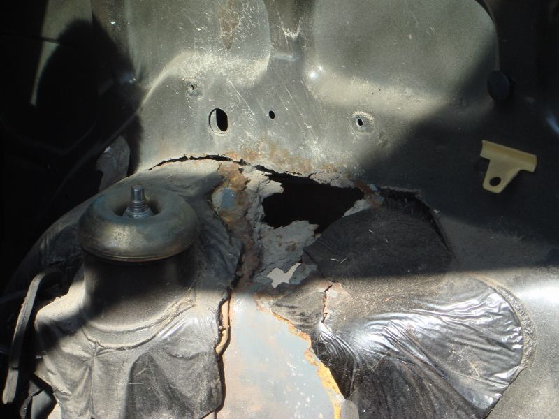 Rusted metal chassis with a shock mount and a hole showing damage