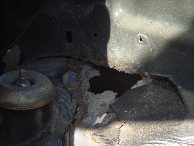 Rusted wheel well with hole showing suspension component