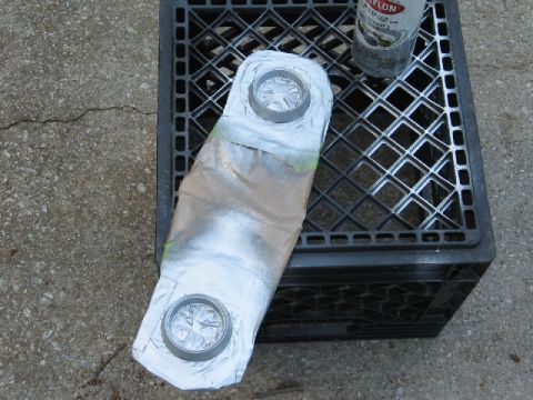 1966 Ford F-100 - A part is being spray painted silver on a black plastic crate outdoors.
