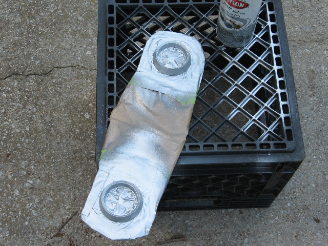 part covered in tape and foil, being spray painted silver on a black crate