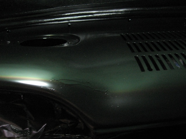 Dark green painted metal panel with a circular hole and horizontal vent slots