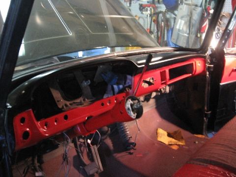 1966 Ford F-100 - The dashboard and steering column of a vehicle are visible, with the dashboard painted red and the steering column removed.