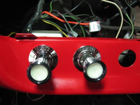1966 Ford F-100 - Close-up of a red dashboard panel showing two vintage chrome pull switches and a complex wiring harness above.