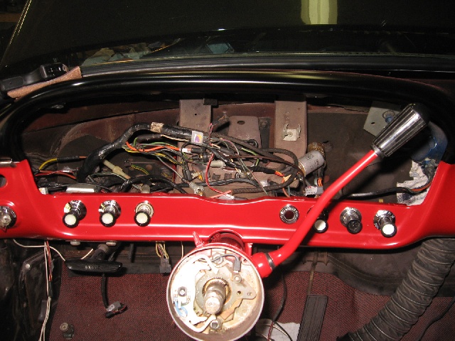 Vehicle dashboard with exposed wiring and red painted dash panel. Steering column is visible