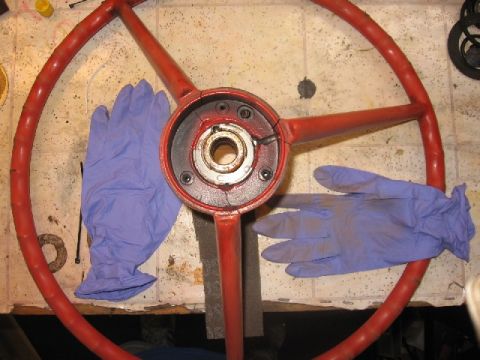 1966 Ford F-100 - Red steering wheel part with cracked center hub and blue gloves on a workbench.