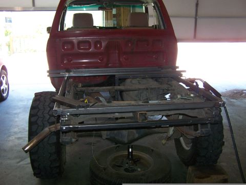 1988 Suzuki Samurai - The rear chassis of a red pickup truck is visible, with its frame and large tires exposed.