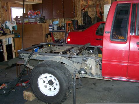 1988 Suzuki Samurai - A red pickup truck is undergoing a custom bed frame modification in a workshop setting.