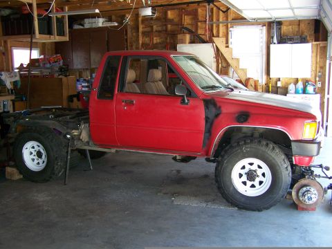 1988 Suzuki Samurai - This red pickup truck is in a garage, with its rear section removed and front fender showing primer.