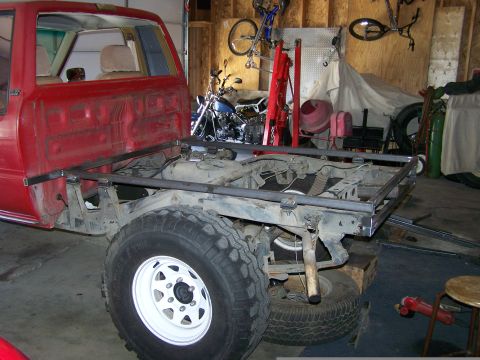 1988 Suzuki Samurai - A red pickup truck's frame is being modified with new metalwork in a cluttered garage setting.