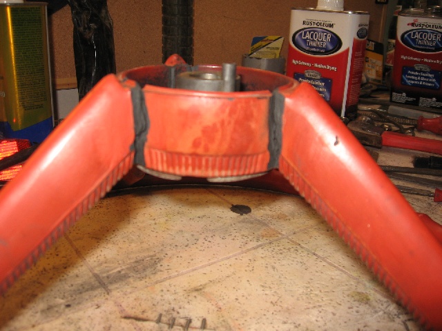 Red steering wheel hub with black rubber seals, on a workbench with cans of lacquer thinner