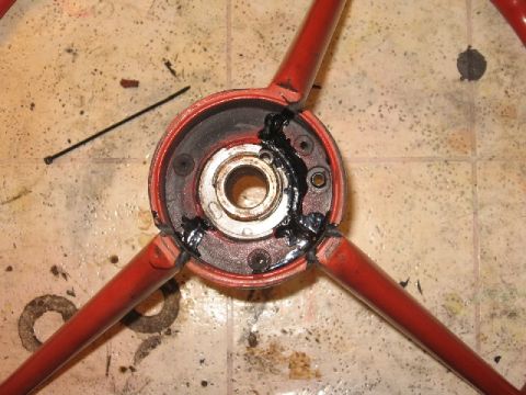 1966 Ford F-100 - Close-up of a red steering wheel hub, showing the central bearing and grease, with three spokes visible.