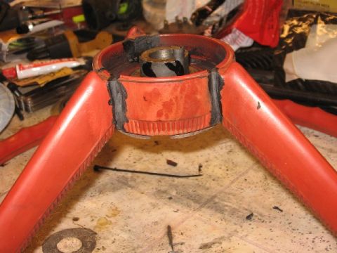 1966 Ford F-100 - A red powder-coated or painted tubular metal component with a central cylindrical hub/collar exposing a bore, set on a cluttered workbench…