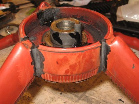 1966 Ford F-100 - Close-up of a red steering wheel hub, showing damage and black sealant around the central metal shaft.