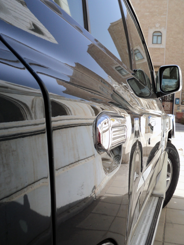 Close-up of black SUV's glossy side panel with chrome handle and mirror reflecting buildings