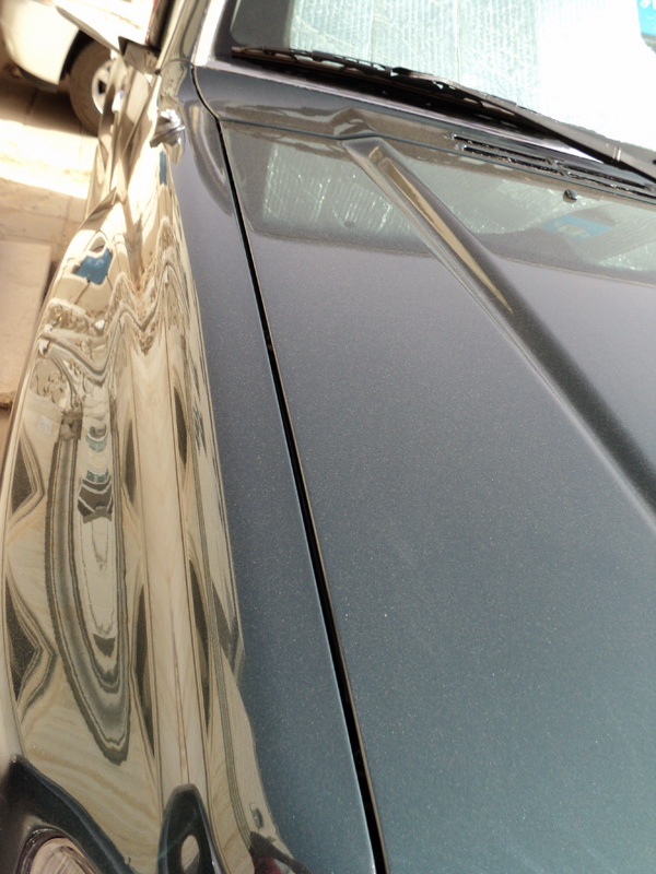 Close-up of dark gray metallic car hood showing glossy vs dull paint sections