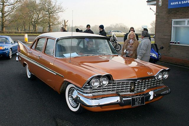 Orange 1959 Plymouth Belvedere sedan with a white roof, parked next to a blue car and a motorcycle