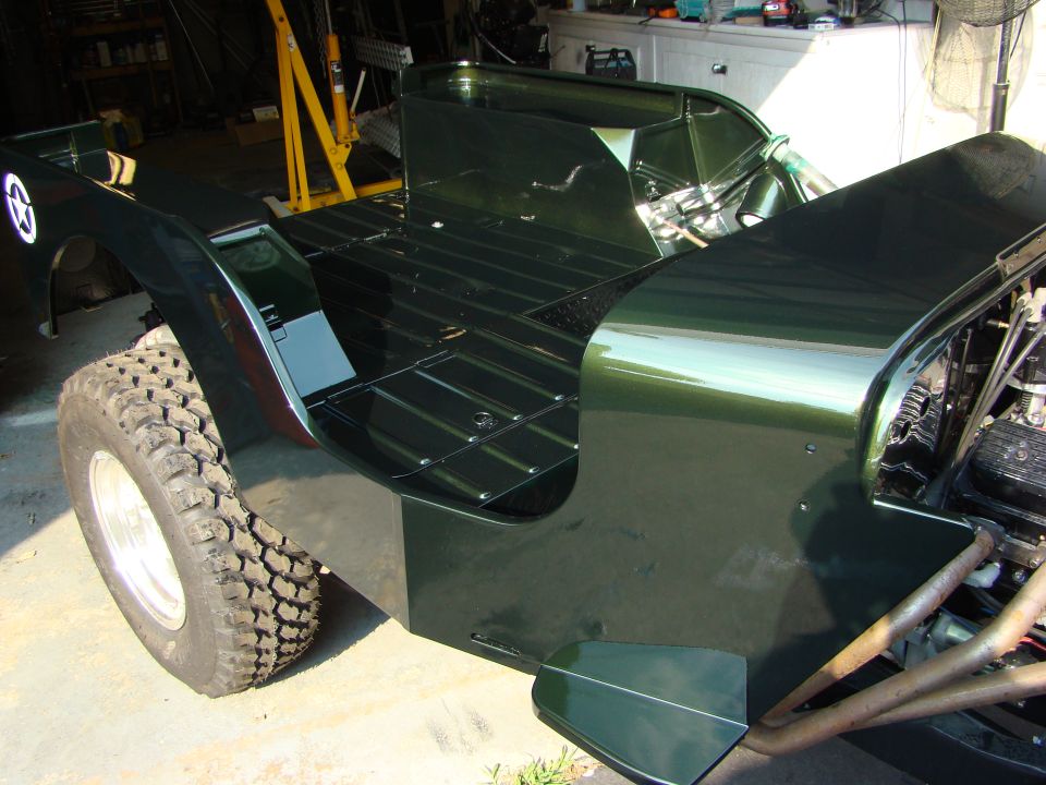 Dark green Jeep CJ-3A body, showing the flatbed and front fender with a star emblem. Engine and exhaust visible