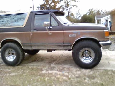 1990 Ford Bronco - Side profile of a brown and black Ford Bronco, showing its distinctive body style and aftermarket wheels.