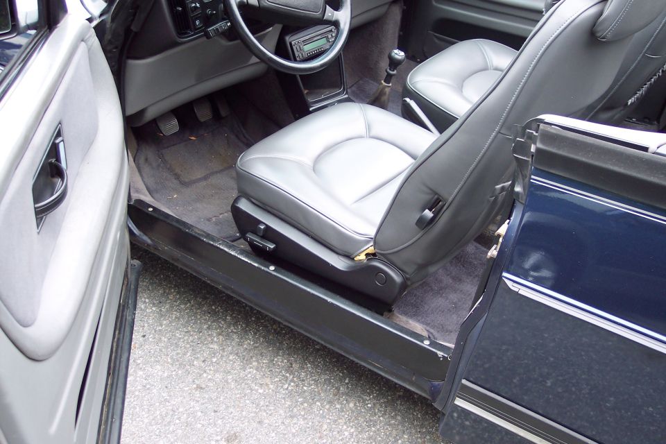 Interior view of a car with gray leather seats, dashboard, and steering wheel. The driver's side door is open