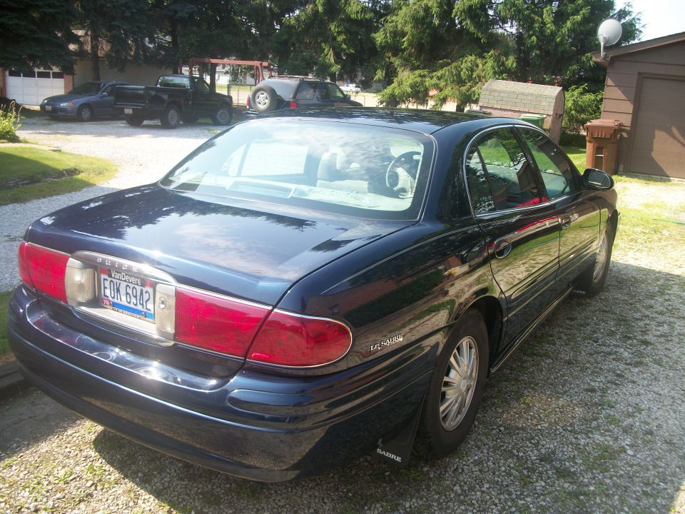 Dark navy Buick LeSabre sedan 3/4 rear on gravel drive with Ohio plate and mud flap