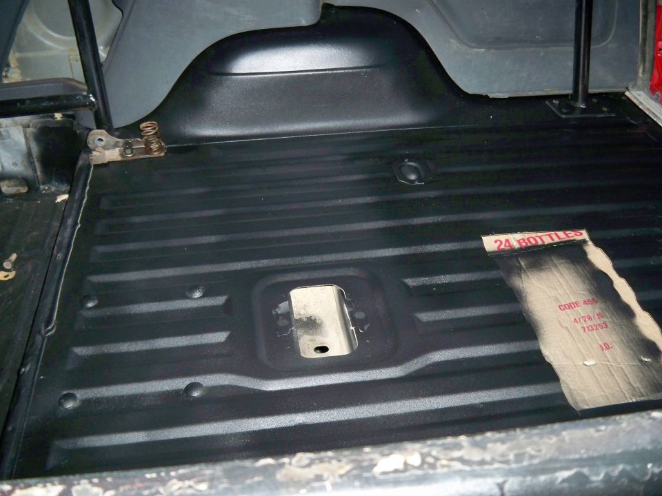 Back of a vehicle with black ribbed flooring. Cardboard with '24 BOTTLES' and some codes is on the floor