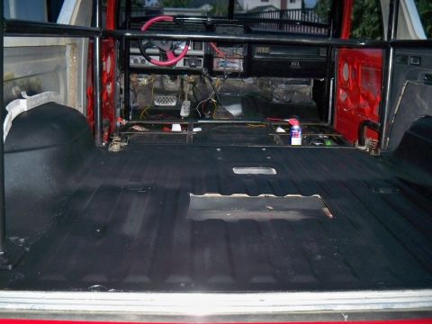 1985 Ford Bronco - The interior of a vehicle shows exposed flooring, a roll cage, and the dashboard with wiring.