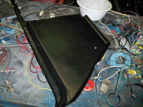 1985 Ford Bronco - A black plastic trim piece lies on a workbench amidst a tangle of wires and electrical components.