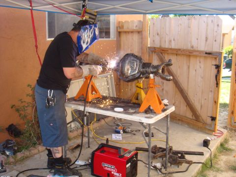 1992 Ford Bronco - A person in a welding mask works on a vehicle axle assembly outdoors.
