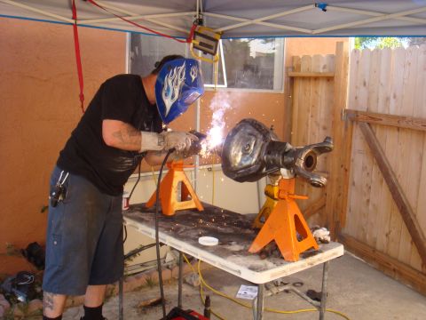 1992 Ford Bronco - Man welding a vehicle axle on jack stands outdoors.