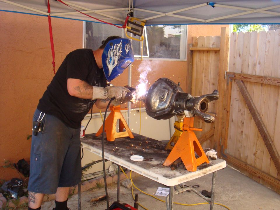 Man in welding mask working on a vehicle axle supported by jack stands