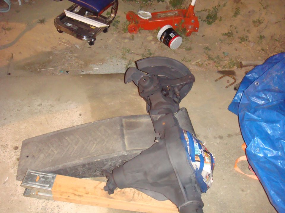 Ford Bronco rear axle assembly on wooden blocks, with a blue tarp and red jack in background