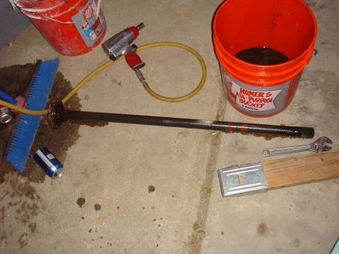 1992 Ford Bronco - A drive axle lies on the floor next to tools and buckets, suggesting a repair or maintenance scene.