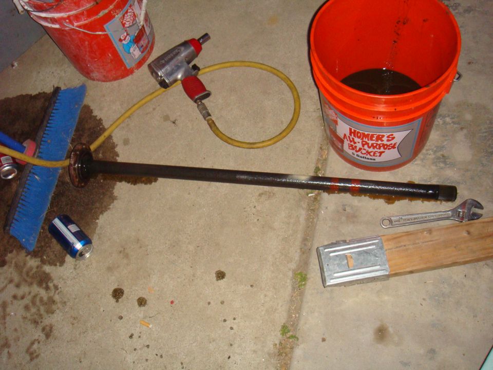 Drive axle with a blue brush, impact wrench, and two buckets on a concrete floor
