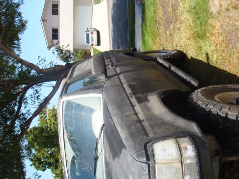 1992 Ford Bronco - This black Ford Bronco is parked outside a house with a tree in the foreground and a garage in the background.