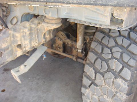 1992 Ford Bronco - Close-up view of the front axle and suspension system, including the shock absorber and coil spring, alongside a off-road tire.